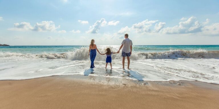 man, woman and child holding hands on seashore