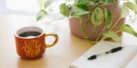 black retractable pen on opened book beside red and white go get'em-printed coffee cup