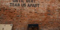 Until debt tear us apart printed red brick wall at daytime