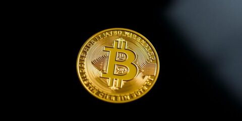 Close-up of a gleaming Bitcoin coin on dark background.