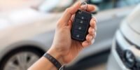 Hand holding car key with blurred modern car background.